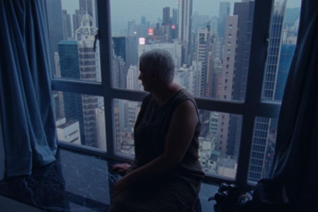 Anke Bak silhouetted in front of a window revealing the Hong Kong skyline, in a scene from WOOD AND WATER.